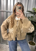 Person wearing a beige sweater with white patterns, taking a mirror selfie.
