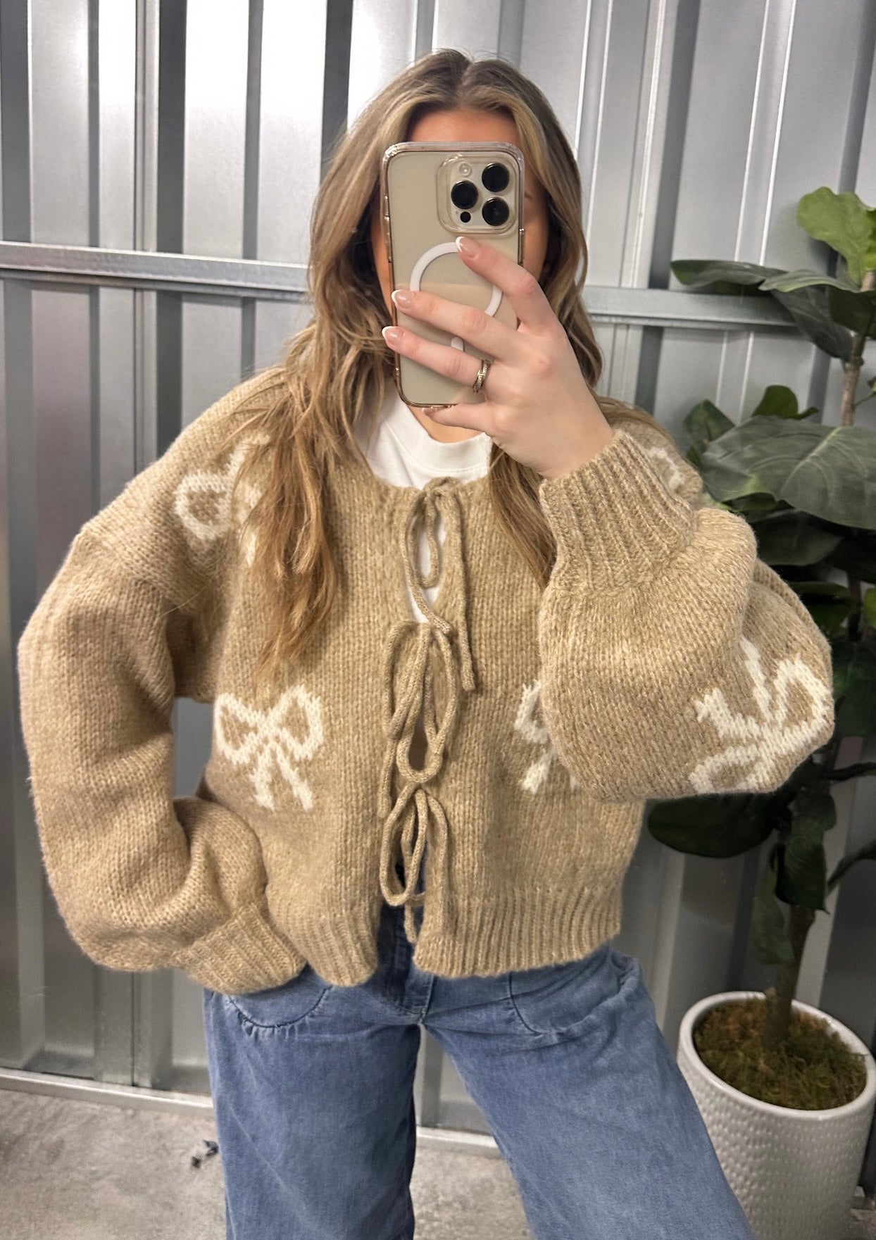 Person wearing a beige sweater with white patterns, taking a mirror selfie.