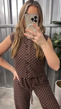 Woman taking a mirror selfie wearing a brown polka dot jumpsuit.