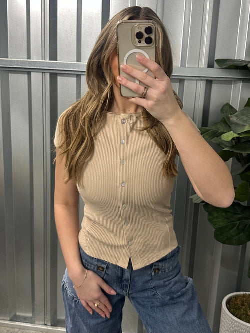 Person wearing a beige ribbed sweater and blue jeans, standing indoors.