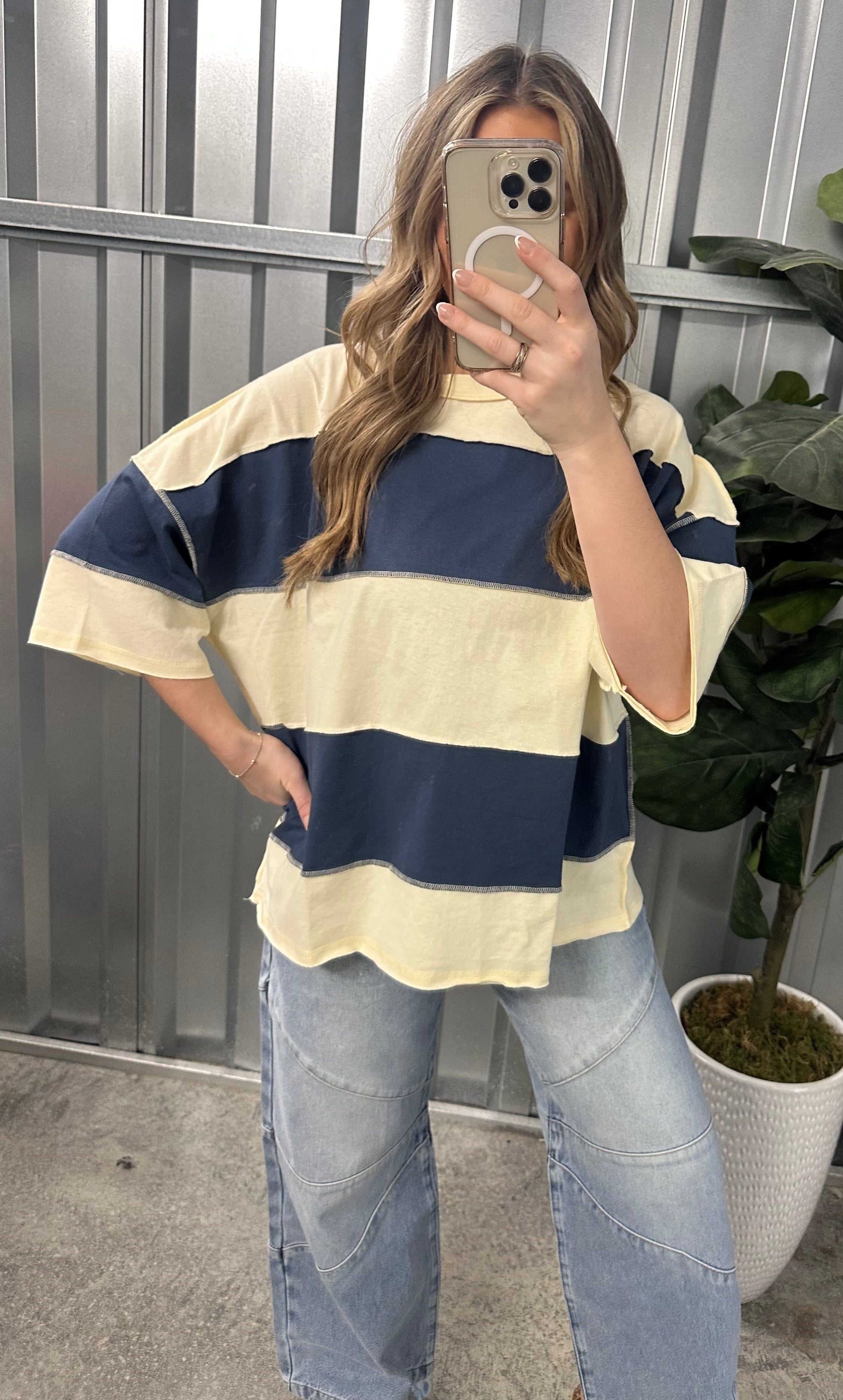 Person wearing a striped shirt and jeans taking a mirror selfie outdoors.