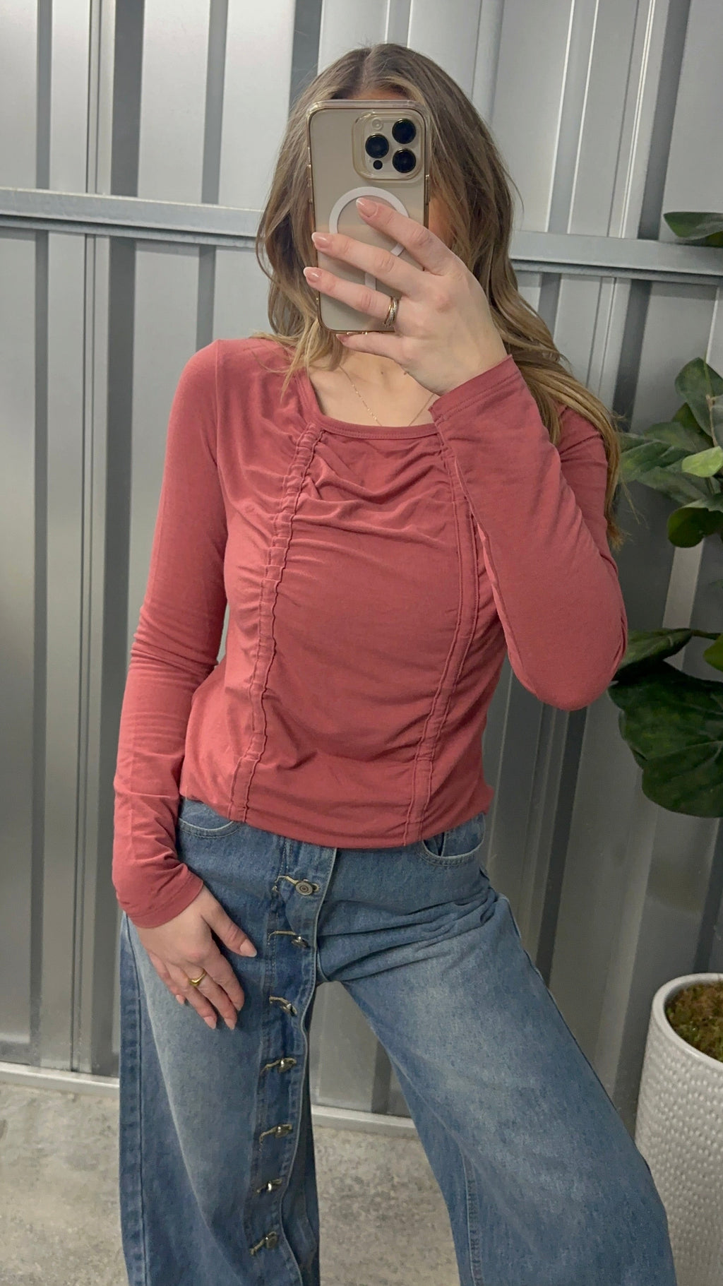 Person wearing a pink long-sleeve top and blue jeans taking a mirror selfie.
