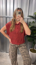 Person wearing a red sleeveless top and patterned pants taking a mirror selfie.