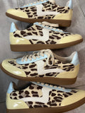 Pair of leopard print sneakers with beige soles on a gray floor.