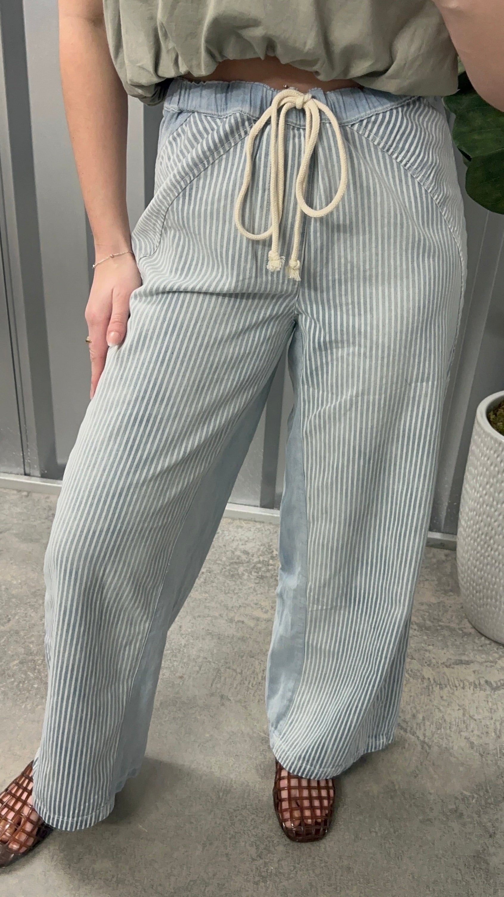 Person wearing light blue striped pants with a drawstring, standing indoors.