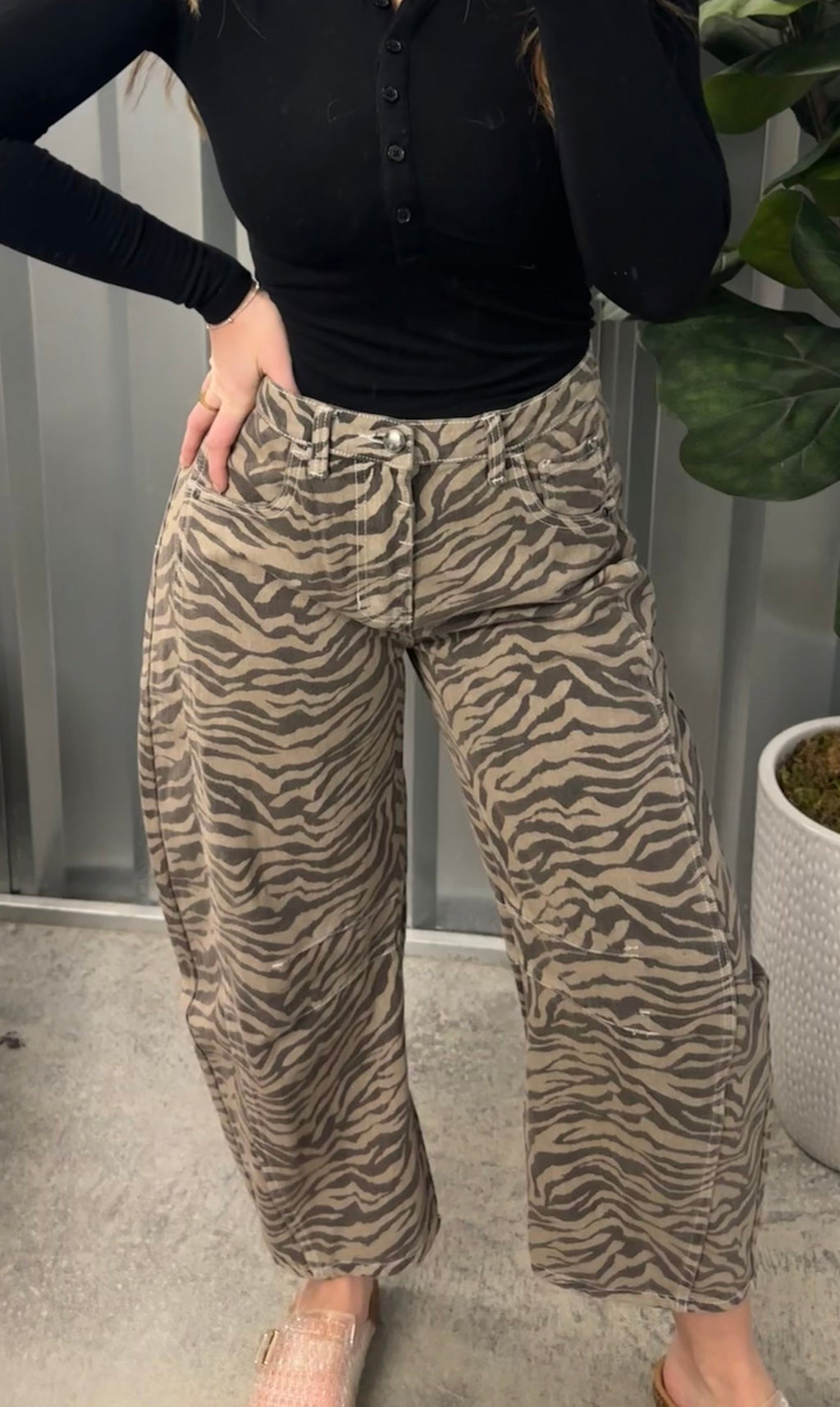 Person wearing a black top and zebra print pants standing indoors with a plant in the background.