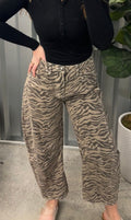 Person wearing a black top and zebra print pants standing indoors with a plant in the background.