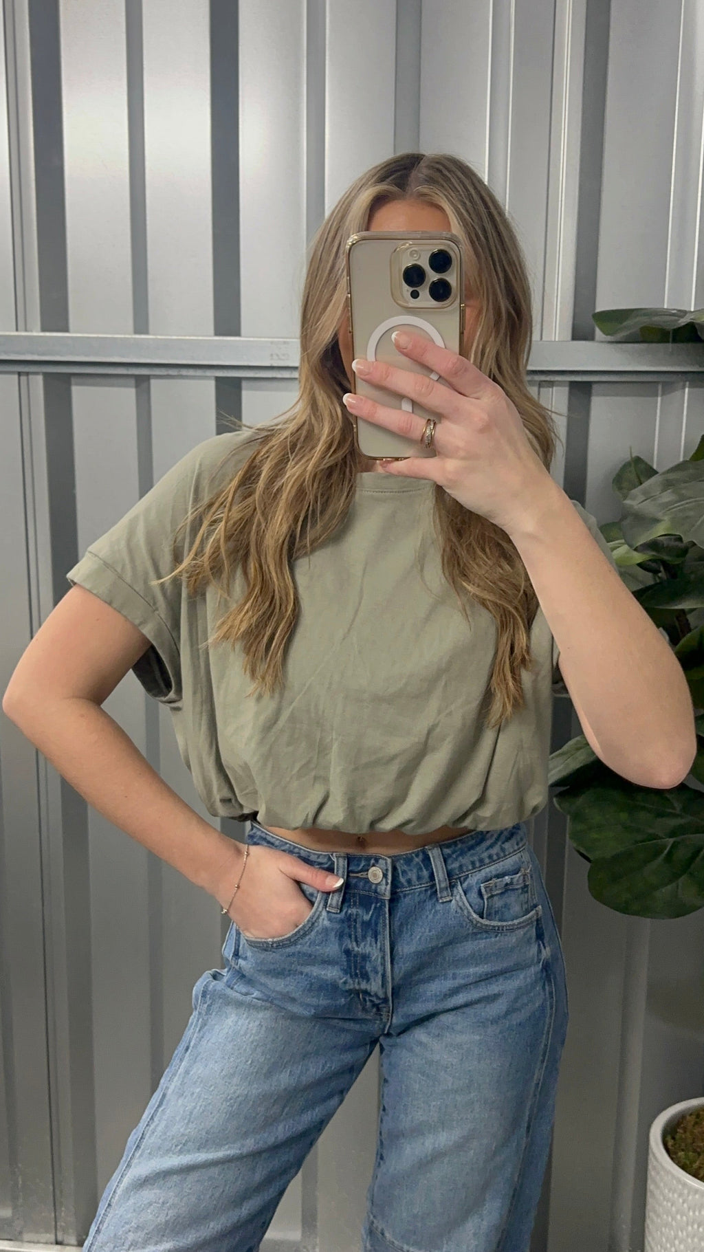 Person wearing a green crop top and blue jeans taking a mirror selfie.