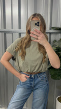 Person wearing a green crop top and blue jeans taking a mirror selfie.