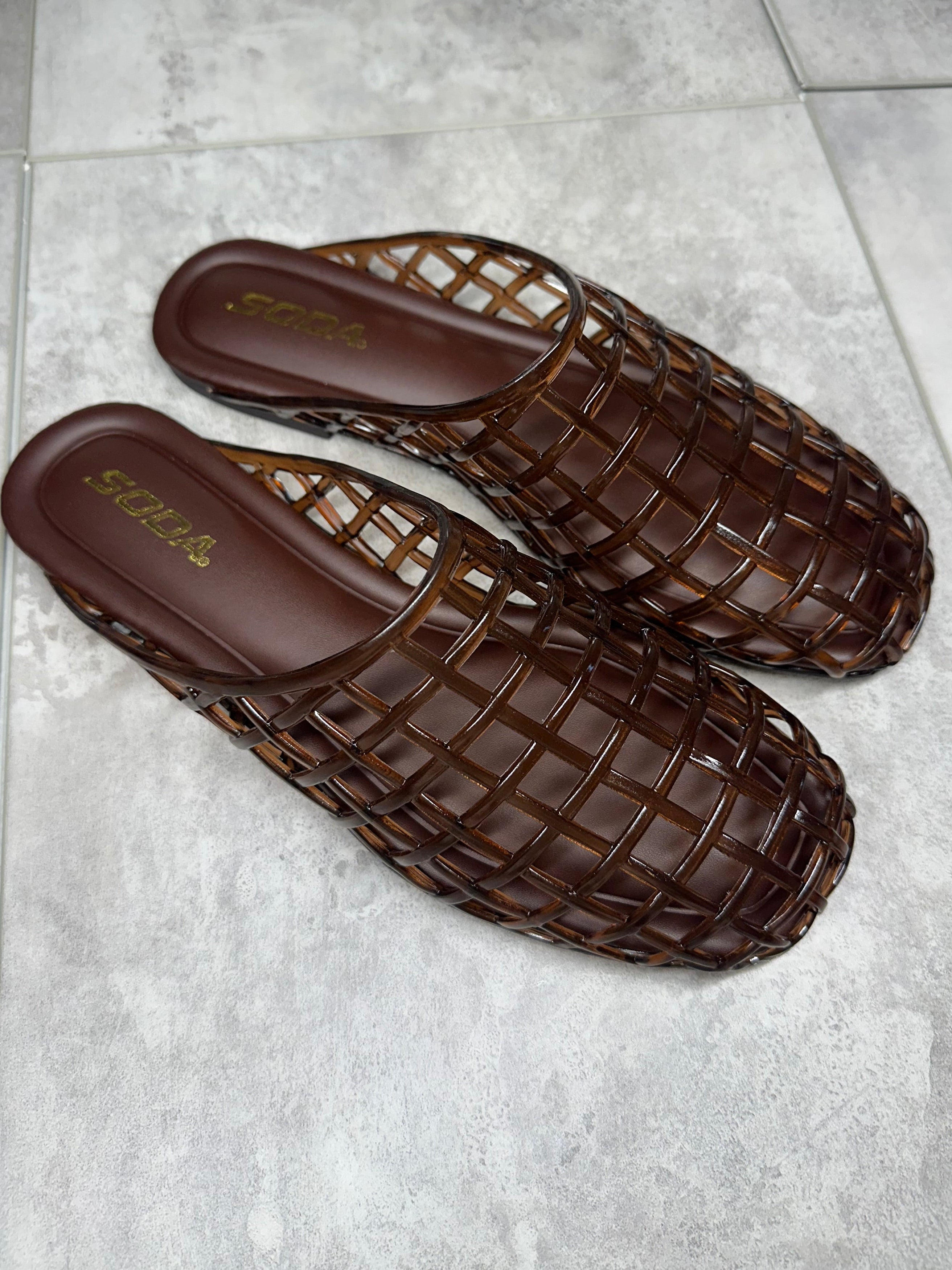 Pair of brown woven sandals on a gray tiled floor