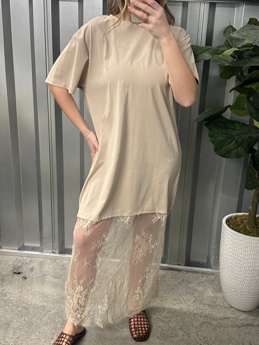 Woman wearing a beige dress with lace details standing in front of a metal shutter.