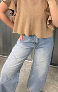 Person wearing a brown cropped sweater and light blue jeans, taking a mirror selfie.